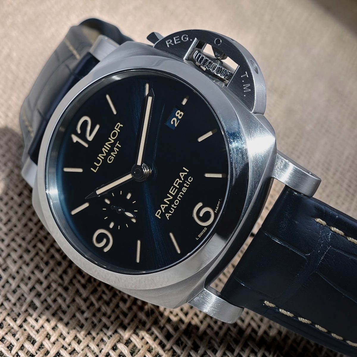Panerai Luminor GMT PAM01033 angled view showing blue dial, polished steel bezel and blue stitched strap