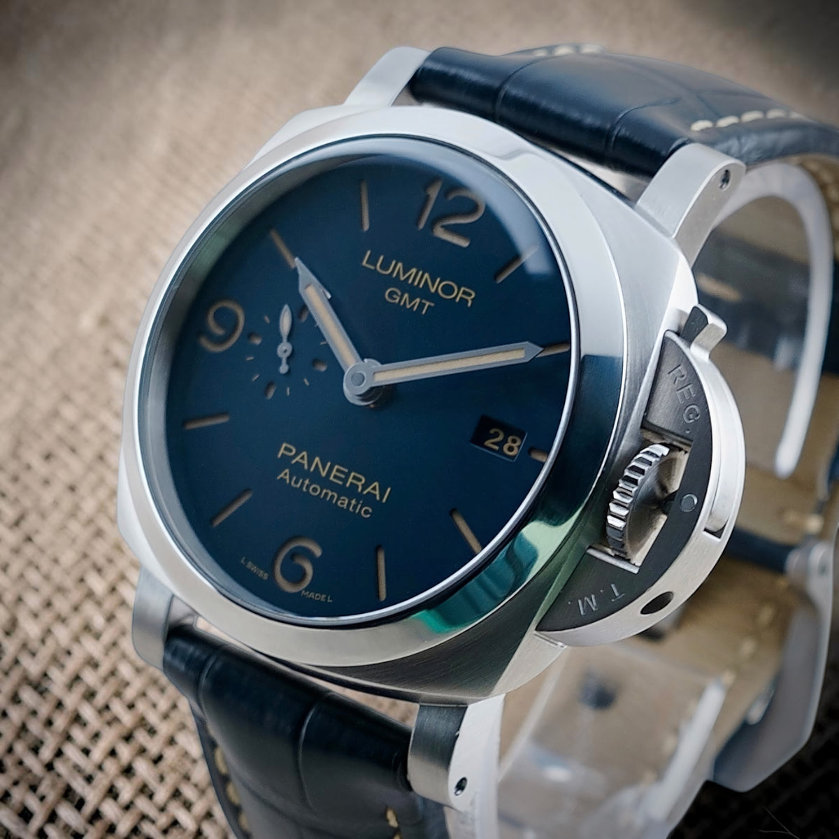 Panerai Luminor GMT PAM01033 crown-side view with blue sun-brushed dial and stainless steel crown-protection bridge