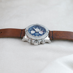 Wrist Flex Timepieces Breitling Super Avenger chronograph with blue dial and brown leather strap on a neutral surface