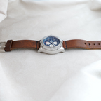 Wrist Flex Timepieces Breitling Super Avenger chronograph with blue dial and brown leather strap on a neutral fabric.